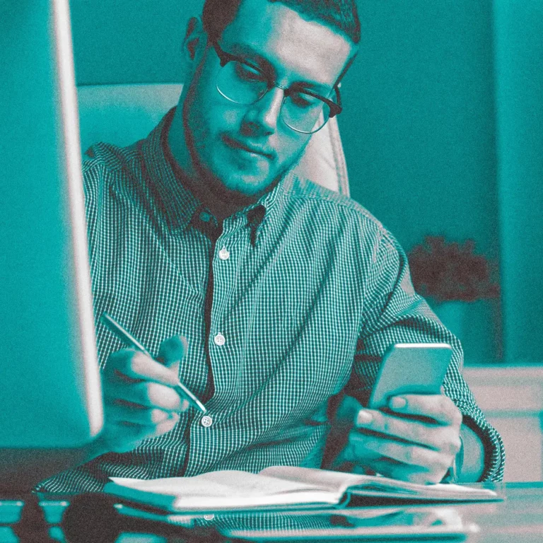 man at desk looking at phone taking notes